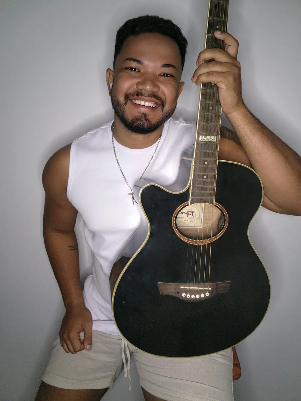 Jeff Moreira sorrindo, segurando um violão preto
